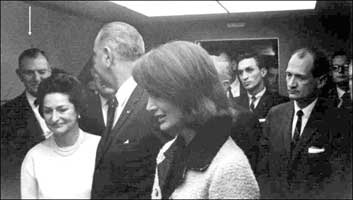 Mission accomplished....Standing next to a "mourning" Jackie, LBJ gets a wink and a smile from Congressman Albert Thomas. His wife, Lady Bird, is smiling by his side. 